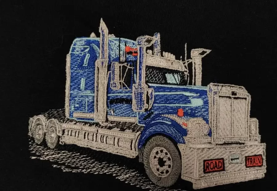 Camion brodé en bleu et beige sur fond noir, inscription Road Train à l'avant.