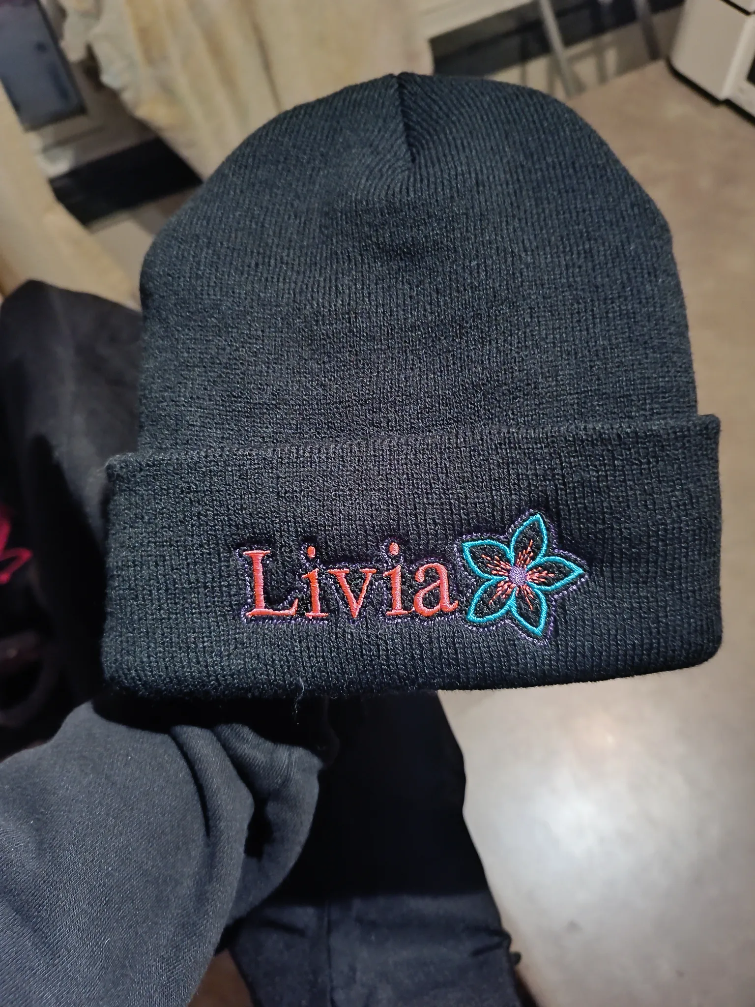 Tuque noire personnalisée avec le prénom Livia et une fleur brodés.